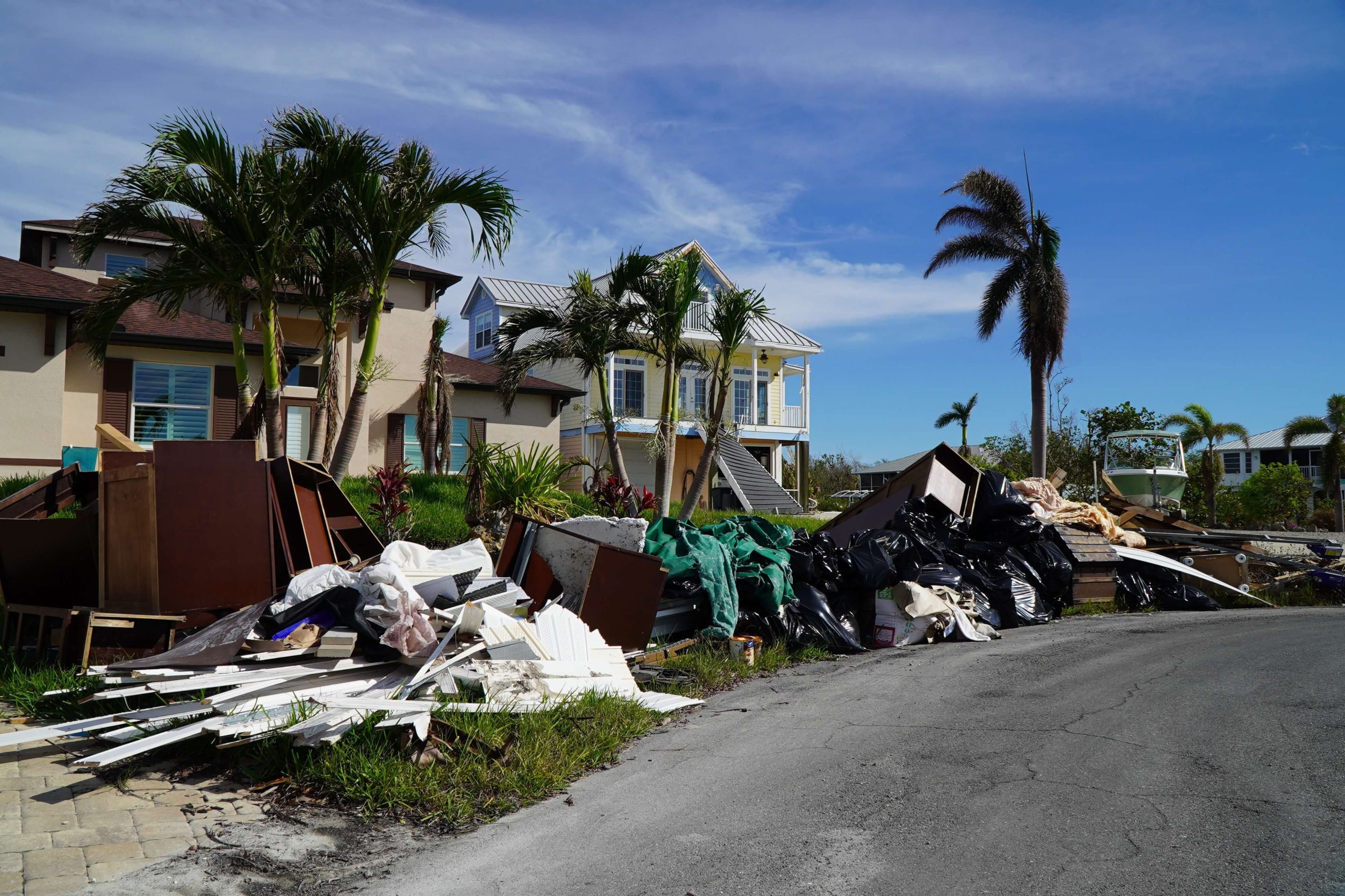 Escombros incluyendo muebles amontonados en la calle listos para ser recogidos. Unas residencias de color amarillo se encuentra detrás de los escombres– solo una de las estructuras que quedaron paradas en Fort Myers Beach después del huracán Ian. (Jiahui Huang/Columbia Journalism Investigations)