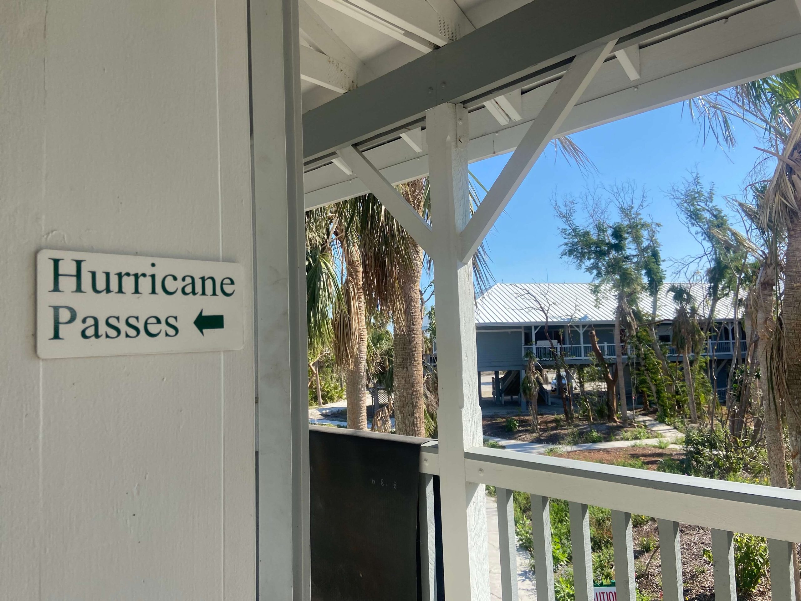 A white sign with black letters that reads “Hurricane Passes” hangs outside Sanibel City Hall. The damage from Hurricane Ian’s wind can be seen in the battered trees in the background. Sanibel officials limited access to the wealthy community by issuing hurricane passes to workers involved in the recovery effort. (María Inés Zamudio/ Center for Public Integrity)